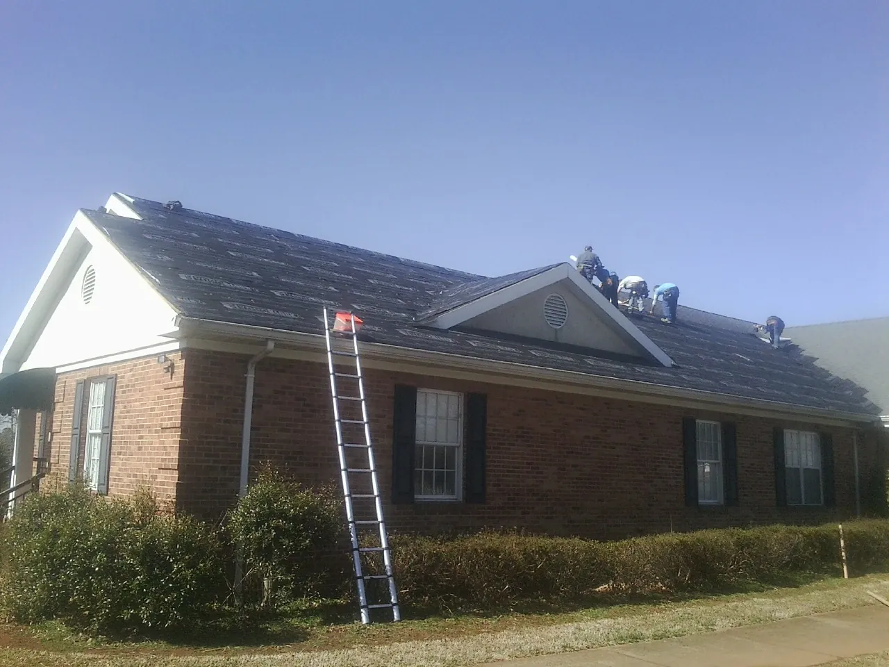 Crew tearing shingles off a brick ranch roof with a ladder set — Emergency Roof Repair work by our crew in Deer Grove