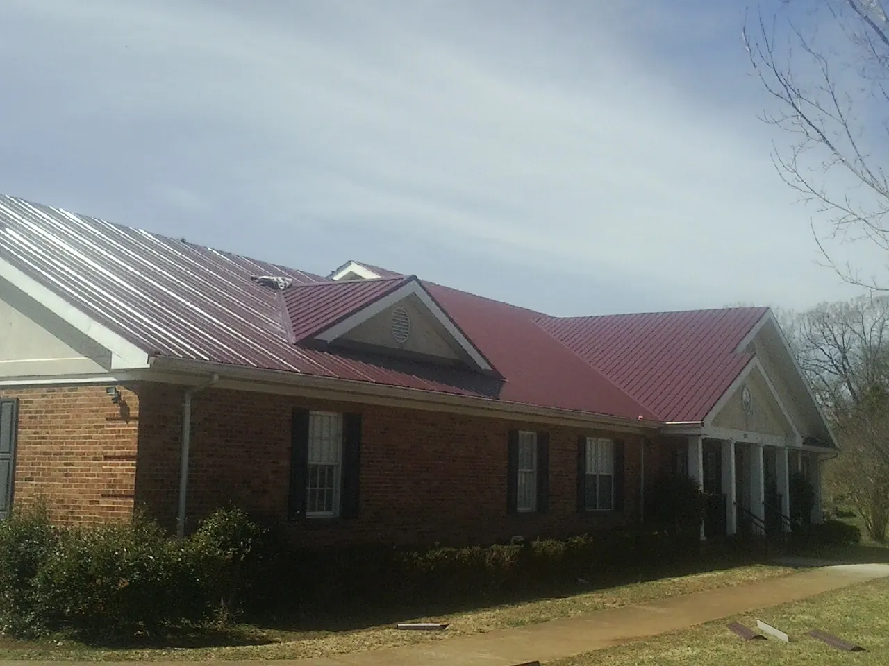 Red metal roof with gabled entries on a long brick building, from a Hail Damage Roof Repair job in Deer Grove