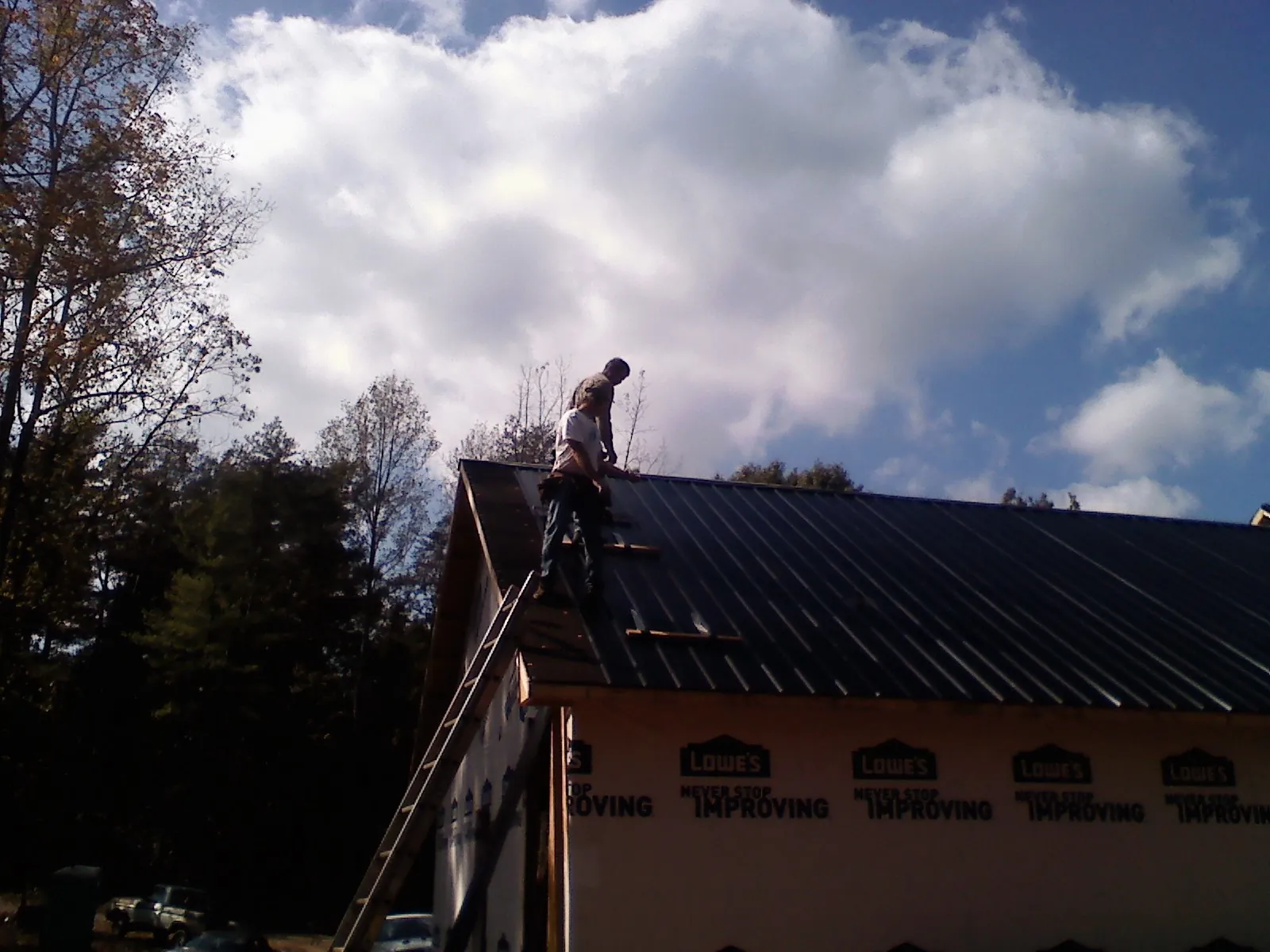 Roofer fastening dark metal panels high against a cloudy sky, from a Roof Inspection job in Deer Grove