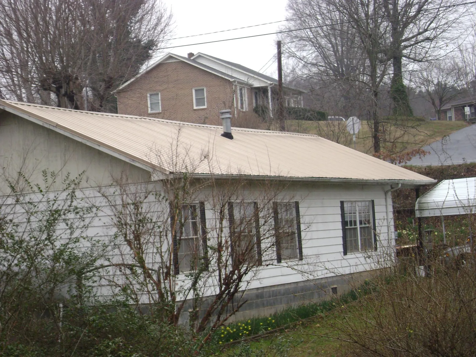 Tan metal roof on a white sided house set into a hillside — Commercial Roofing by Roofing Brothers in Deer Grove